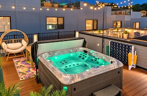 A hot tub on a wooden deck with a chair and a table, surrounded by string lights. - Music City Escape w/Rooftop Hot Tub & Pool! 11 Beds (Nashville)