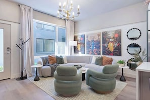 Ein modernes Wohnzimmer mit einer Couch, Sesseln, einem Couchtisch, einer Stehlampe und Kunstwerken an den Wänden.