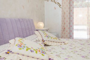 A neatly made bed with floral bedding and decorative pillows, a bedside lamp, and a wall with a floral pattern.