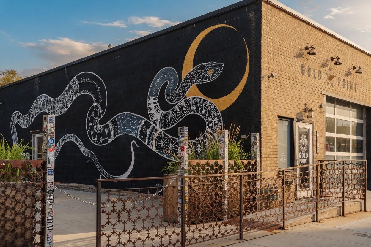 Un edificio con un mural de una serpiente y una luna creciente, un letrero que dice 'Gold Point' y una entrada protegida por una reja.