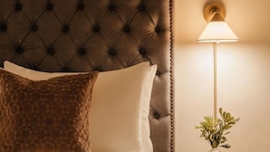 A neatly made bed with a tufted headboard, a bedside lamp, a small table with a plant, and a wicker basket on the bed. - Ceros (Denver)