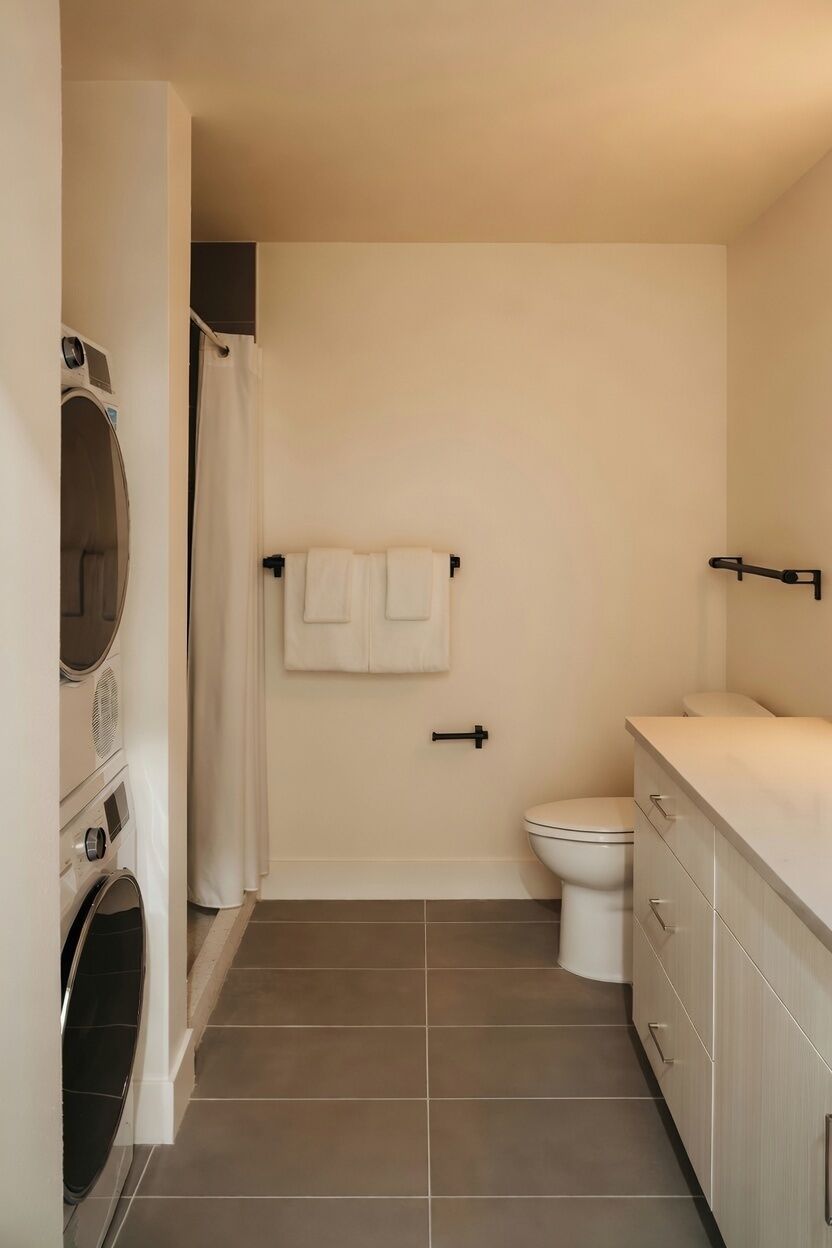 A compact bathroom with a toilet, a washing machine, and a shower area.