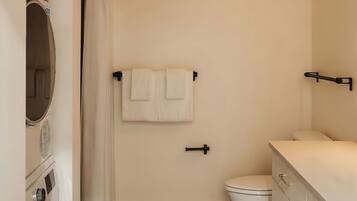 A compact bathroom with a toilet, a washing machine, and a shower area.