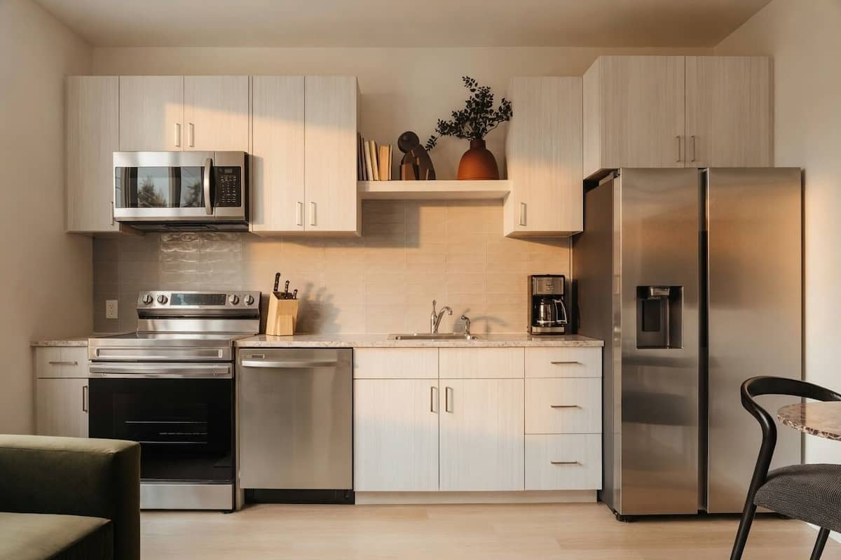 Una cocina moderna con electrodomésticos de acero inoxidable, armarios de madera clara y horno empotrado.