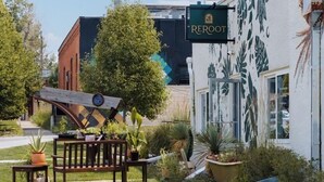 A building with a 'REROOT' sign, a garden with potted plants, a wooden bench, and a clock. - Ceros (Denver)