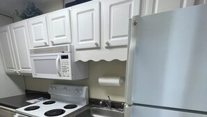 Uma cozinha com armários brancos, pia de aço inoxidável, micro-ondas, fogão e geladeira.