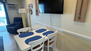 Uma área de refeições com mesa e cadeiras, uma televisão de tela plana na parede e uma luminária de teto.