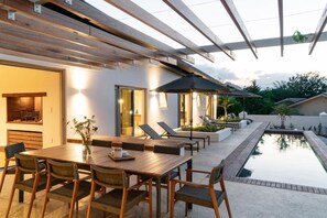 An outdoor patio with a pool, lounge chairs, and a wooden table with chairs. - Luxurious Franschhoek Villa With 3 Bedrooms, 4 Bathrooms, Mountain Views (Franschhoek)