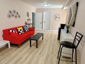 Una sala de estar con un sofá rojo, una mesa de centro negra, un banco blanco y una silla negra.