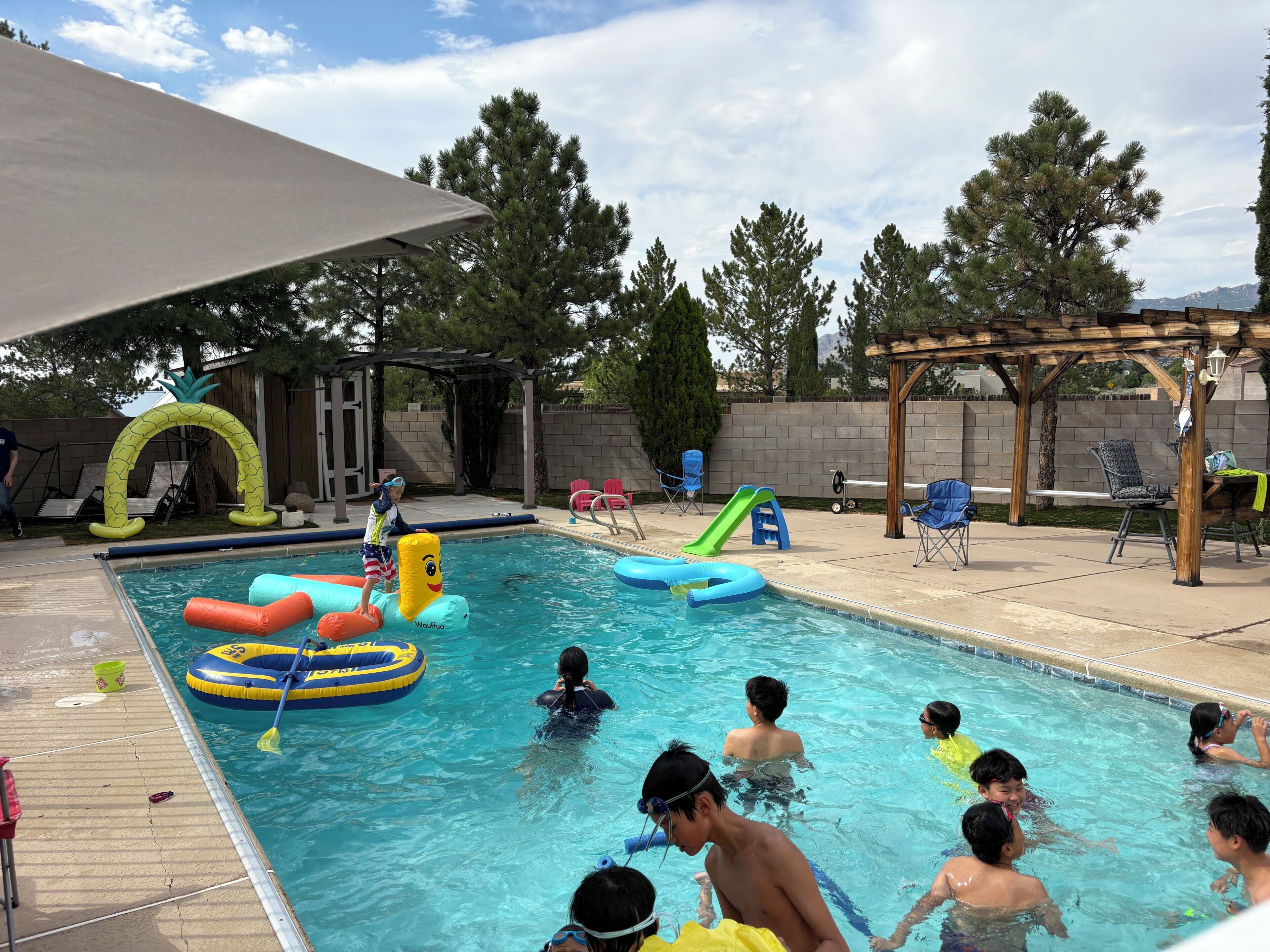 A swimming pool with inflatable toys, lounge chairs, and a pergola.