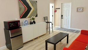 Un espacio habitable compacto con kitchenette, una mesa de comedor, un sofá rojo, una silla negra, un ventilador y un adorno en la pared.