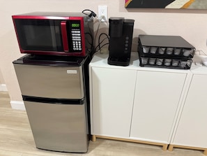 A kitchenette with a stainless steel refrigerator, a red and black microwave, a black coffee maker, and a black basket with cups.