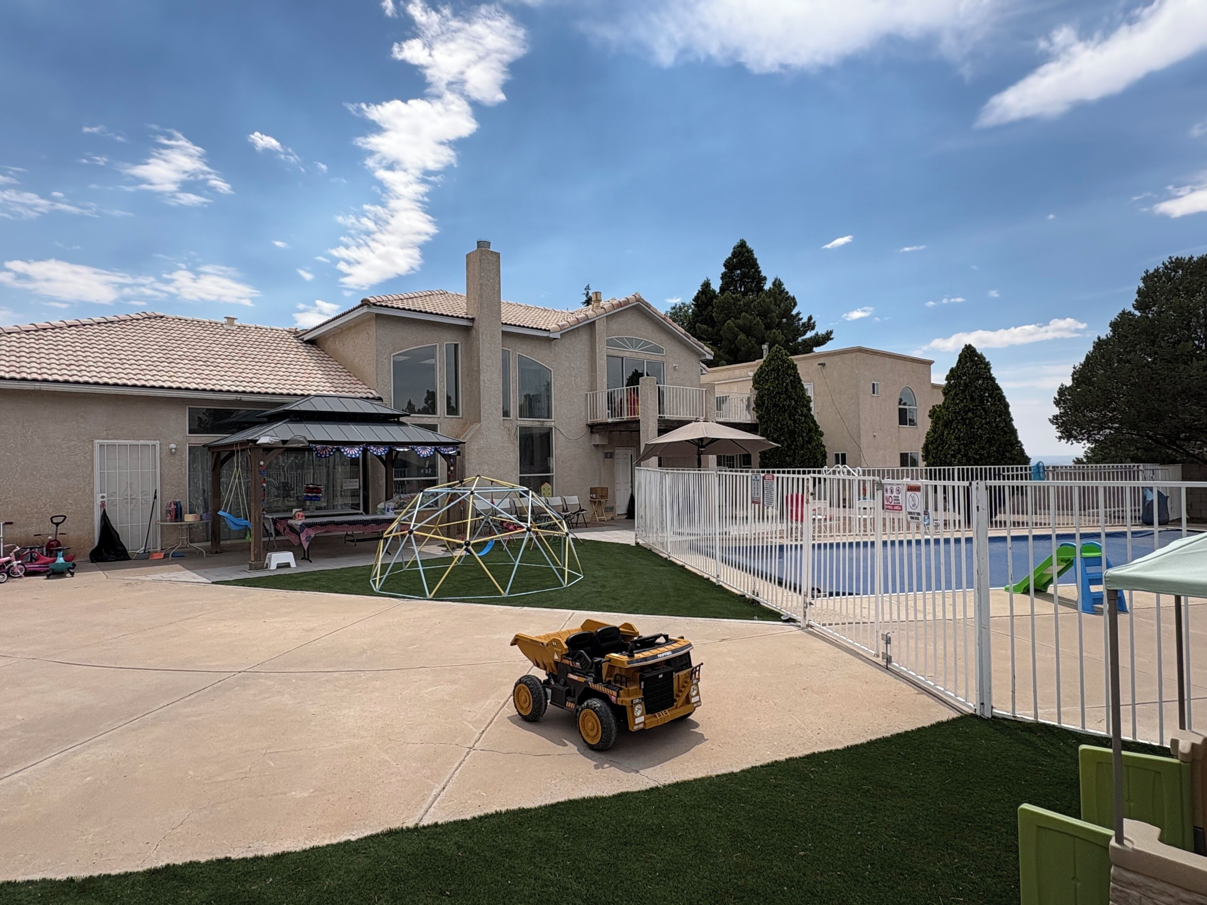 A residential backyard with a swimming pool, a covered patio, and a lawnmower.