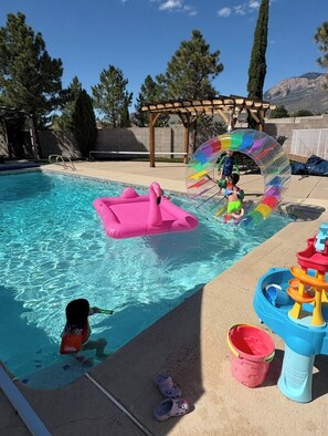 A swimming pool with inflatable toys, a water slide, and a children's play area.