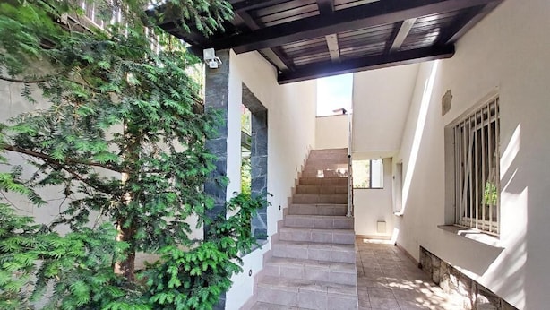Una escalera que sube a un segundo piso, rodeada de follaje y una zona techada.