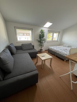 Un espacio habitable compacto con sofá, cama, una mesita y una planta en maceta.