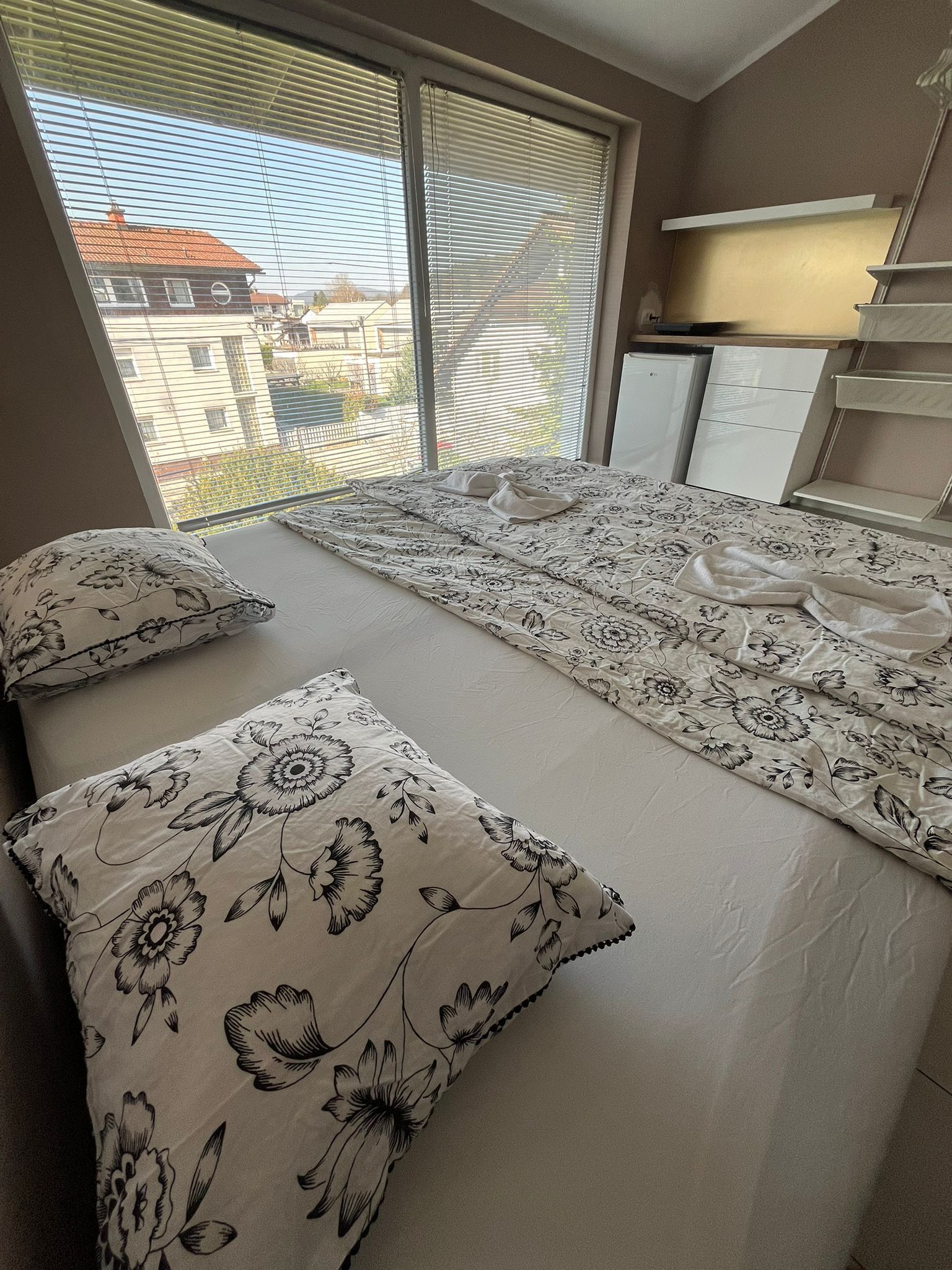 A bedroom with a bed, pillows, a desk, and a window with blinds.
