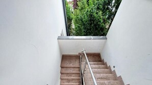 Una escalera con barandilla de metal, paredes blancas y un ventanal pequeño a la izquierda.