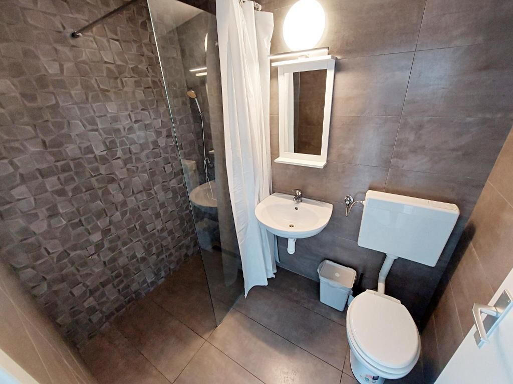A bathroom with a stone wall, a glass shower enclosure, a sink, a mirror, and a toilet.