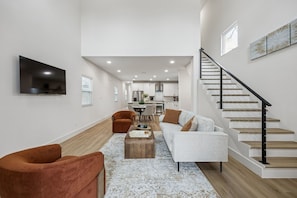 A modern living room with a sofa, armchair, and coffee table, a staircase, and a kitchen in the background. - Modern House with Dallas Skyline Views! (Dallas)