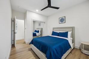 A bedroom with a bed, a ceiling fan, a bedside table, and a door leading to another room. - Modern House with Dallas Skyline Views! (Dallas)
