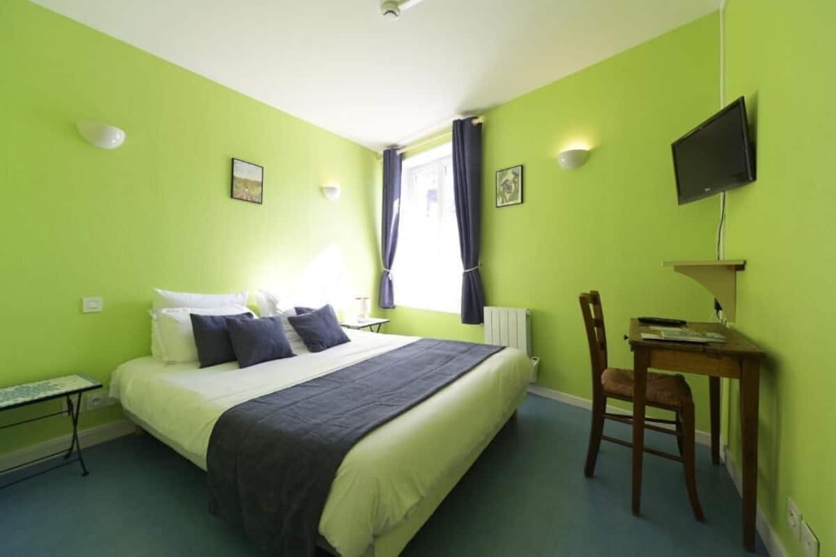 Ein Zimmer mit Bett, Schreibtisch, Sessel, Fernseher und einem fenster mit Vorhängen.