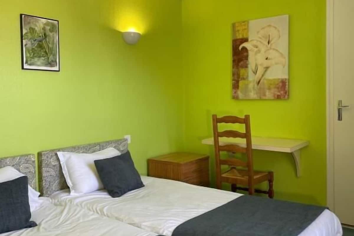 Ein Zimmer mit zwei Betten, einem Schreibtisch, einem Stuhl und Bildern an den Wänden.