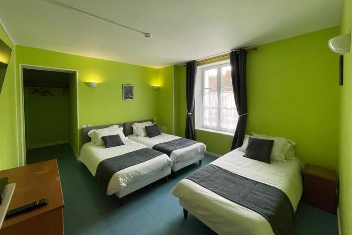 Ein Hotelzimmer mit zwei Betten, einem Schreibtisch, einem Fenster mit Vorhängen und einem Kleiderhaken.