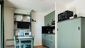 Uma cozinha compacta com área de jantar, uma mesa branca e um sofá cinzento.