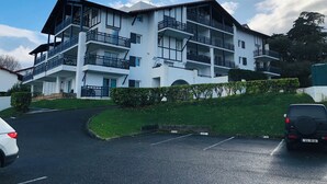 Edifício residencial com vários andares, varandas, área de estacionamento e céu claro.