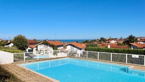 Piscina com cerca branca, rodeada por casas com telhados vermelhos, sob um céu azul límpido.
