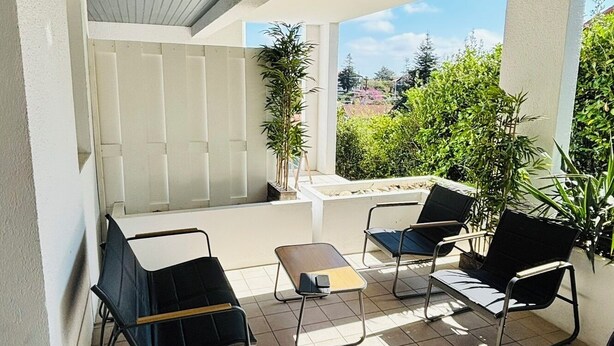 Um pátio externo com piso de azulejos, teto coberto e várias cadeiras e mesas.