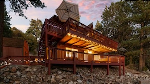 A multi-level wooden cabin with a balcony, string lights, and a large umbrella. - Cozy Cabin, Mountain Views, Hot Tub, Pool Table (Big Bear Lake)