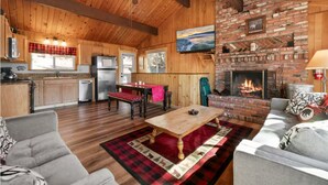 A cozy cabin interior with wooden walls, a fireplace, a television, and a dining area. - Cozy Cabin, Mountain Views, Hot Tub, Pool Table (Big Bear Lake)