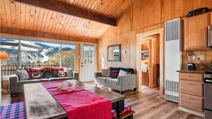 A wooden interior with a dining area, kitchen, and a view of a mountainous landscape. - Cozy Cabin, Mountain Views, Hot Tub, Pool Table (Big Bear Lake)