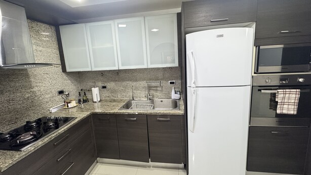 Una cucina moderna con mobili scuri, un frigorifero bianco, un lavello in acciaio inossidabile e un forno integrato.