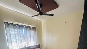 Un dormitorio con cama, ventilador de techo, ventana con cortinas y suelo de baldosas.