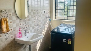 Un baño con lavamanos, espejo, ventana y un electrodoméstico negro.