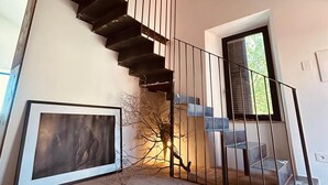 Un interno moderno con soffitto in legno, una scala con ringhiere in metallo, un'opera d'arte incorniciata e una finestra con persiane.