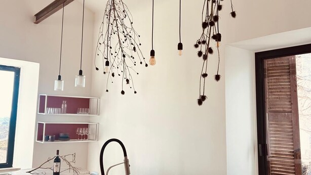 Cucina con piano di lavoro in marmo, lavello incassato, lampade a sospensione e finestra con persiane.