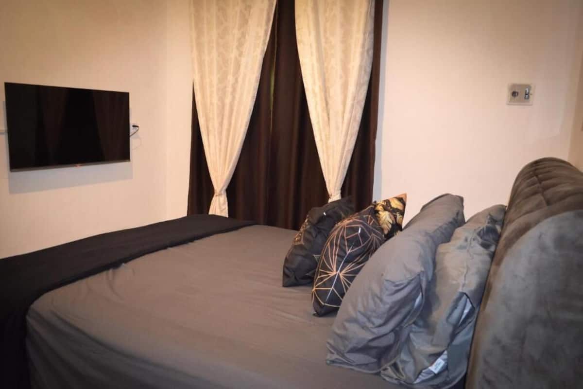 Un dormitorio con cama, cortinas, televisor y enchufe.