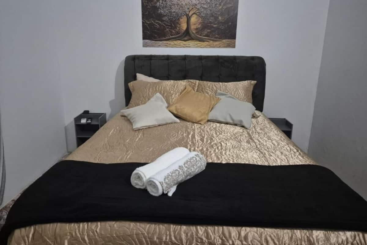 Una cama bien hecha con un cabecero oscuro, un cuadro decorativo encima y una toalla enrollada sobre la cama.