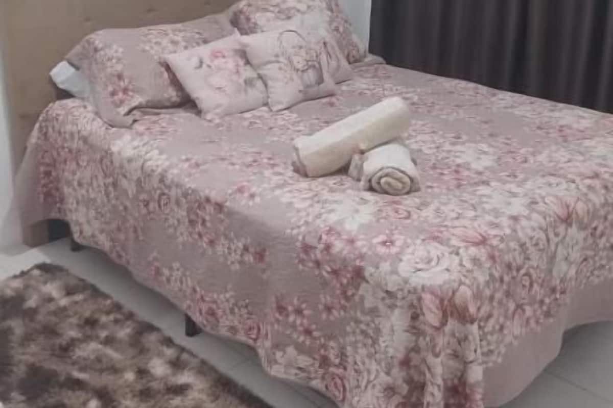 Un dormitorio con cama, cabecera, cuadro, ventana con cortinas y alfombra.