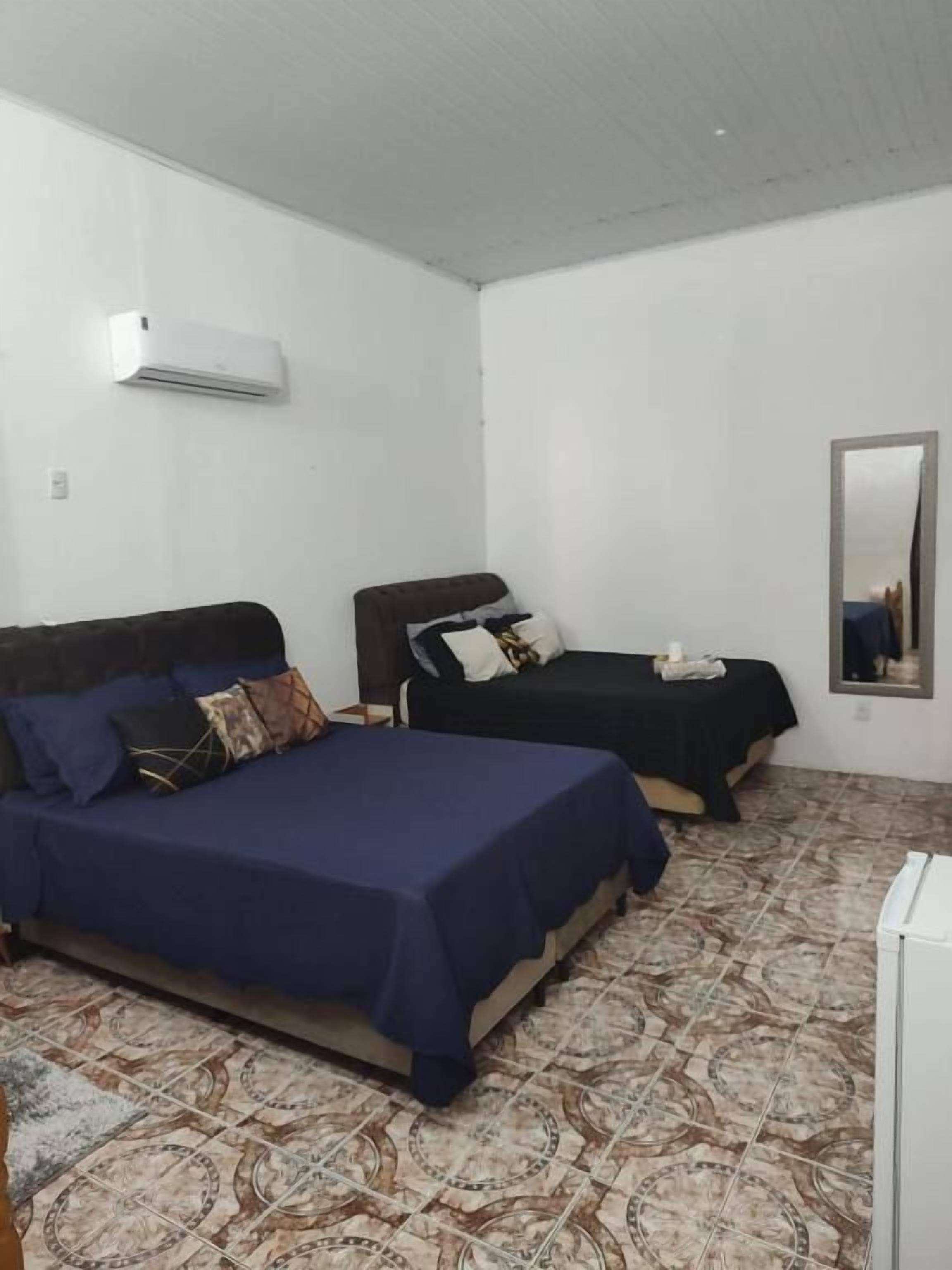 Une chambre avec deux lits, un climatiseur blanc, un miroir et un revêtement de sol à motifs.