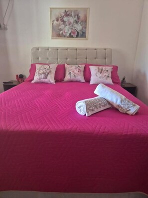 A bed with a pink quilt, a beige headboard, and floral pillows.