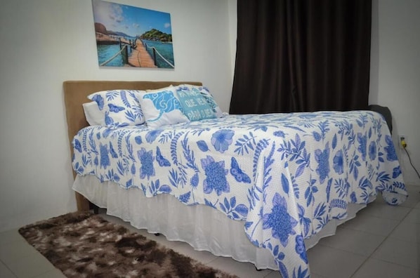 A bedroom with a bed, a pillow, a rug, a wall with a painting, and a curtain.