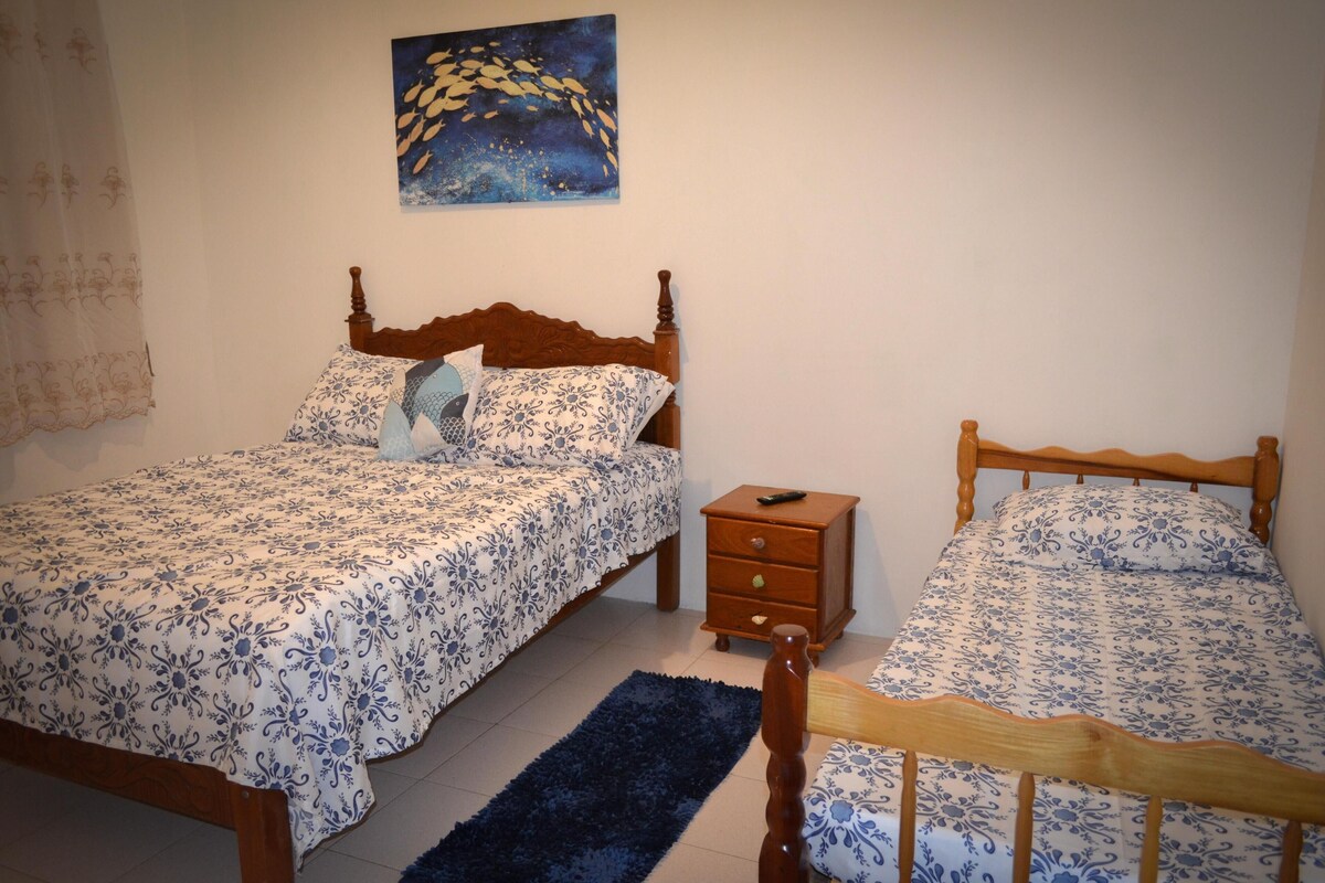 Un dormitorio con dos camas de madera, una mesita de noche, un tapete azul y un cuadro en la pared.