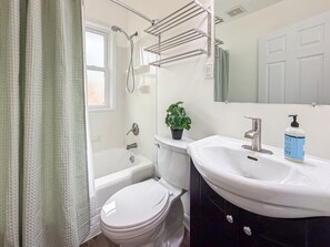 Et badeværelse med badekar, toilet, håndvask og brusearmatur.