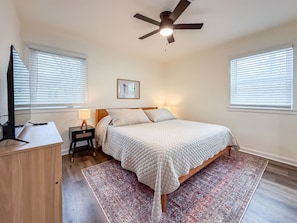 A bedroom with a bed, a ceiling fan, a nightstand, a lamp, and a TV.