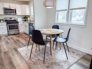 A modern kitchen with white cabinets, a stainless steel stove, and a dining area with a round table and four chairs.